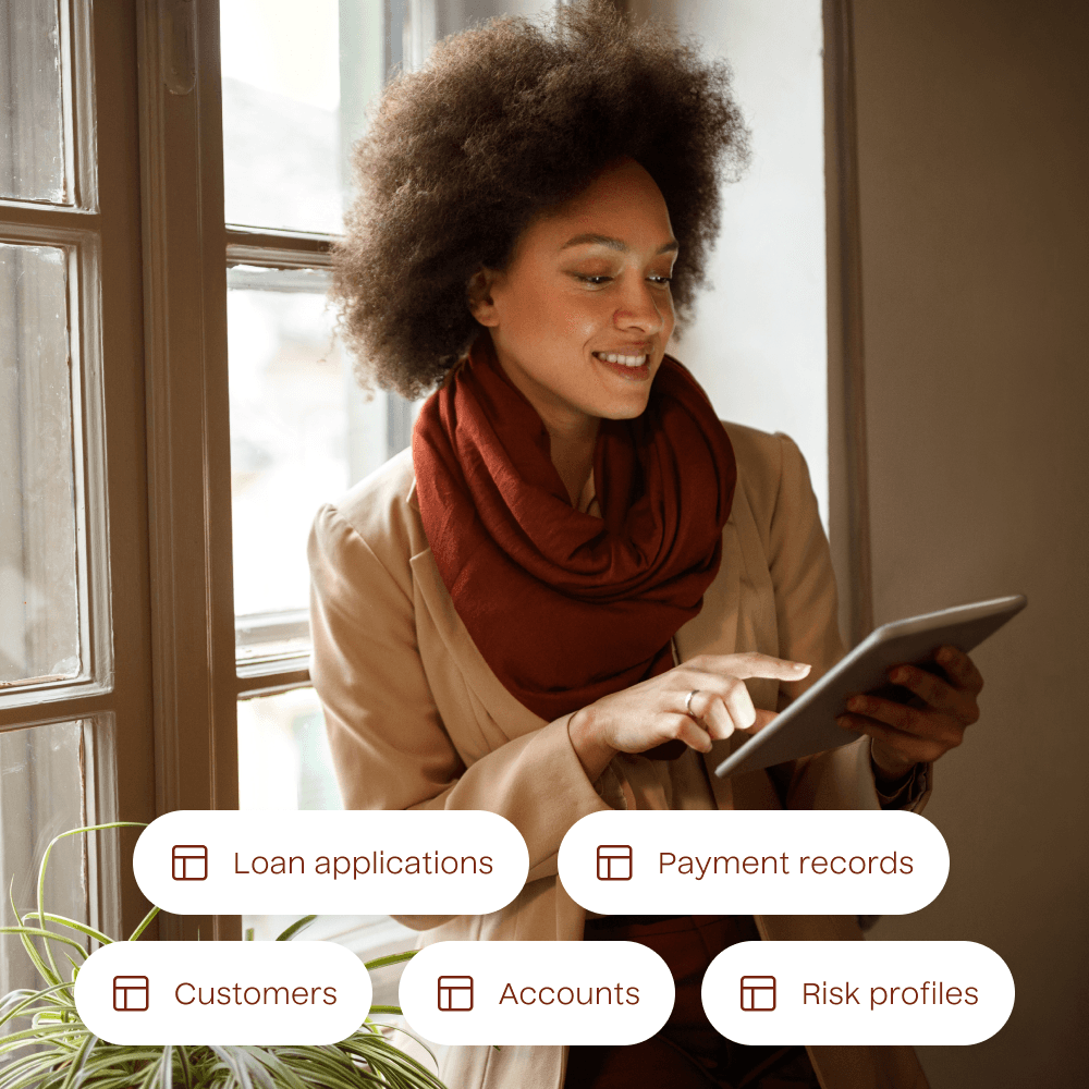A photograph of a person using a tablet with a list of example data tables overlayed. The data tables included are for Loan Applications, Payment Records, Customers, Accounts, and Risk Profiles.
